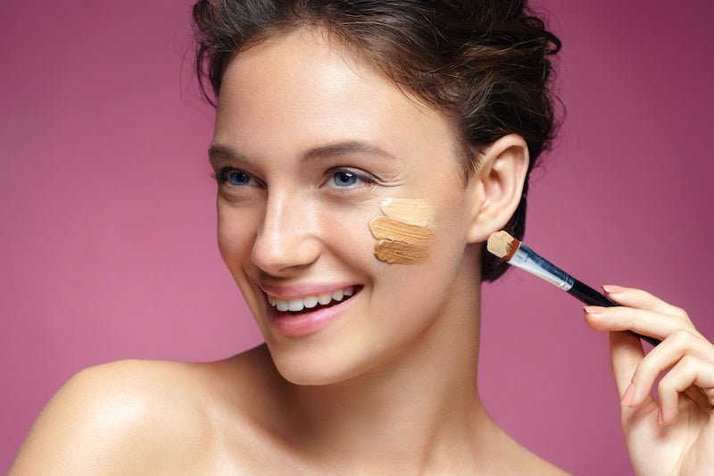 Liquid concealer applied on cheek with small brush; model wearing makeup