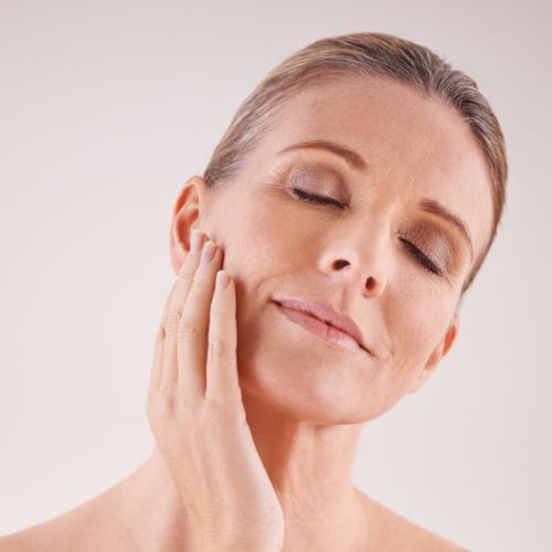 Woman applying vitamin E serum to face and cheek with both hands